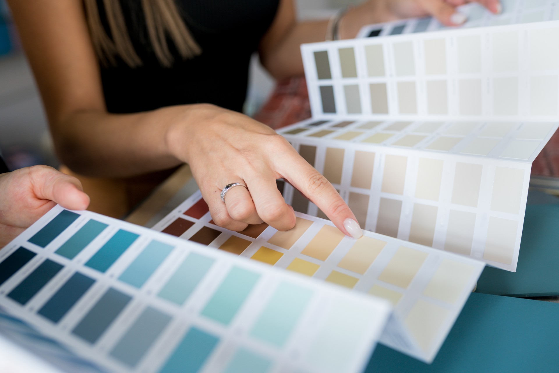 Close-up of two women choosing samples of wall paint. Interior designer consulting a client looking at a color swatch. House renovation concept